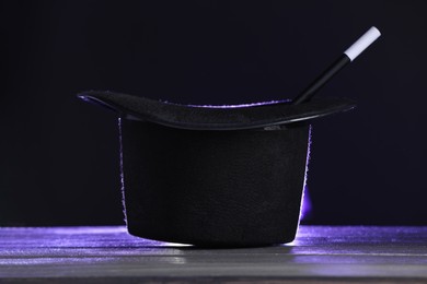 Photo of Magician's hat and wand on wooden table against black background