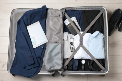 Folded clothes with accessories in open suitcase and shoes on wooden floor, flat lay. Business trip planning