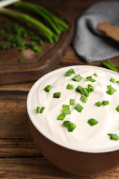 Photo of Fresh sour cream with onion on wooden table, closeup