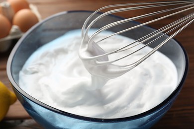 Bowl and whisk with whipped cream on table, closeup