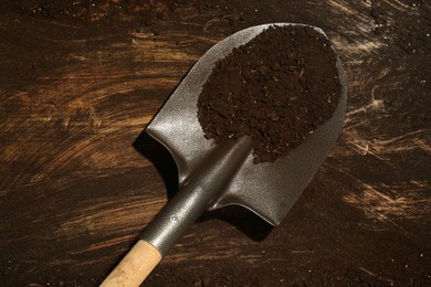 Photo of Metal shovel with fertile soil on dirty wooden surface, top view