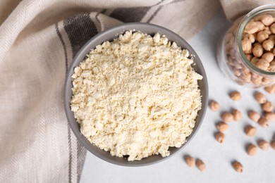 Photo of Chickpea flour in bowl and seeds on light grey table, flat lay