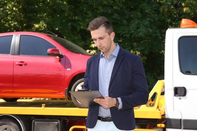 Photo of Man with clipboard near tow truck and broken car outdoors