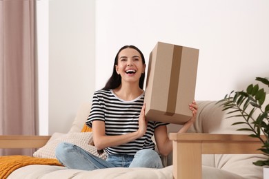 Emotional young woman with parcel on sofa at home. Internet shopping