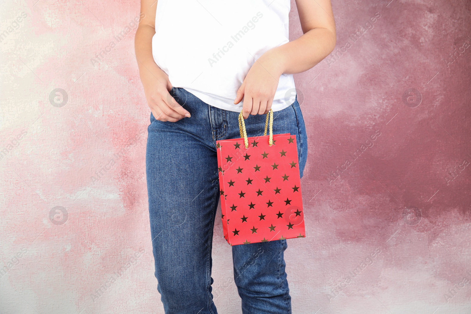 Photo of Woman holding red shopping paper bag with star pattern on pink background, closeup