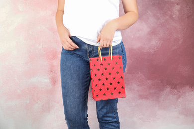 Photo of Woman holding red shopping paper bag with star pattern on pink background, closeup