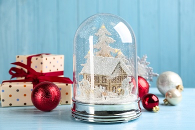 Photo of Beautiful snow globe, gift boxes and Christmas decor on light blue table
