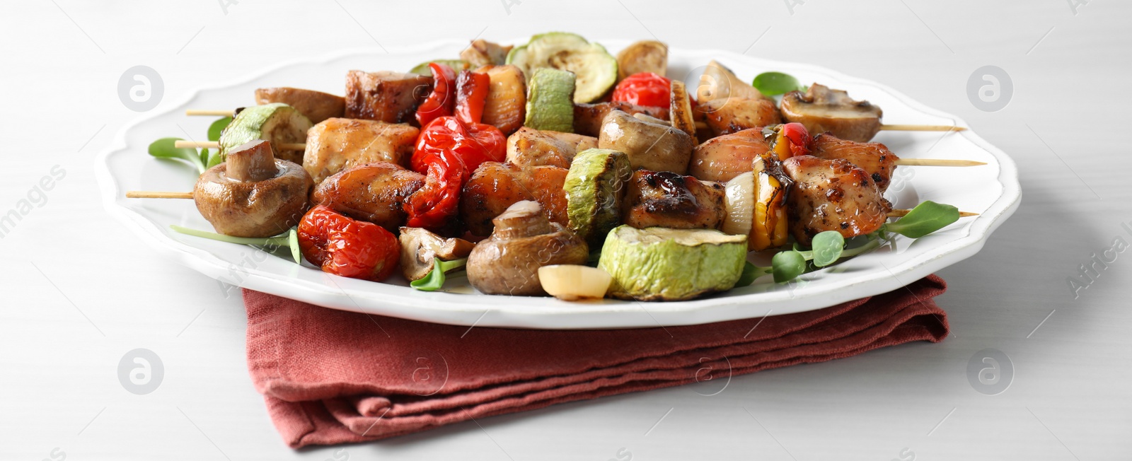 Photo of Delicious shish kebabs with vegetables and microgreens on white table, closeup