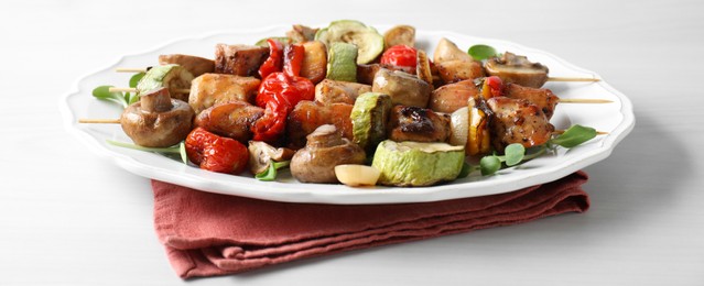 Delicious shish kebabs with vegetables and microgreens on white table, closeup
