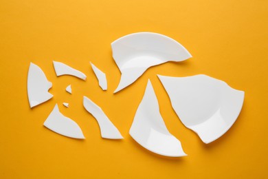 Photo of Pieces of broken ceramic plate on orange background, flat lay