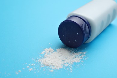 Photo of Bottle and scattered dusting powder on light blue background. Baby cosmetic product