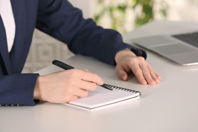 Photo of Woman writing in notebook at white table indoors, closeup