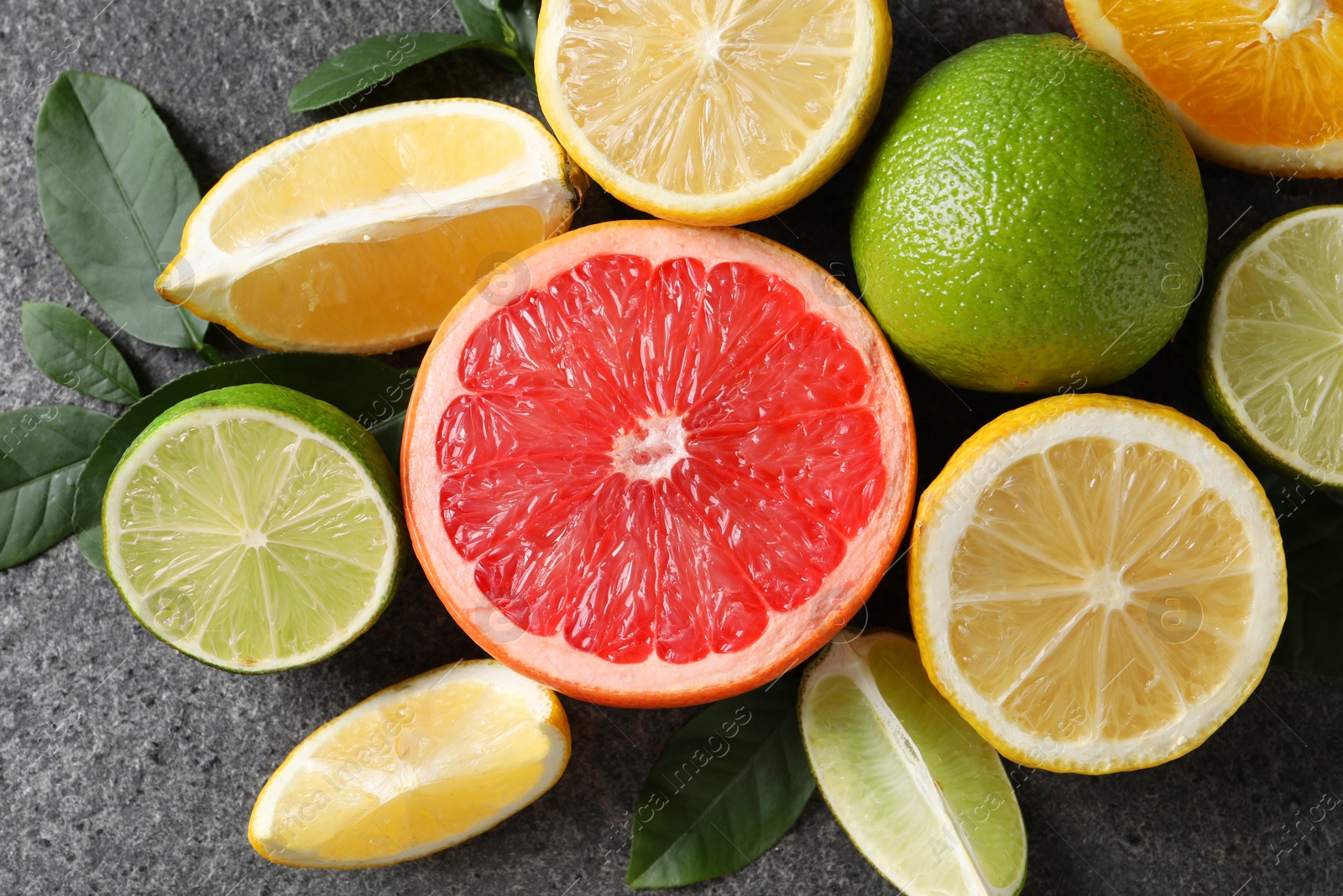 Photo of Different fresh citrus fruits and leaves on grey textured table, flat lay