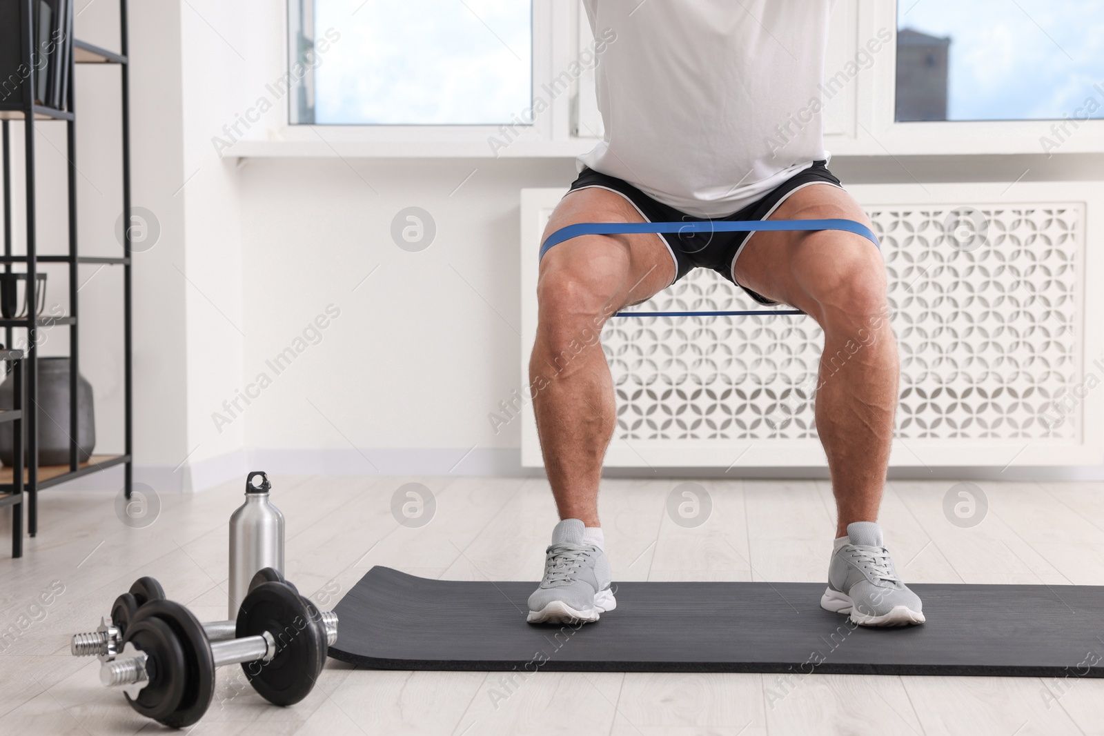 Photo of Athletic man doing exercise with elastic resistance band on mat at home, closeup