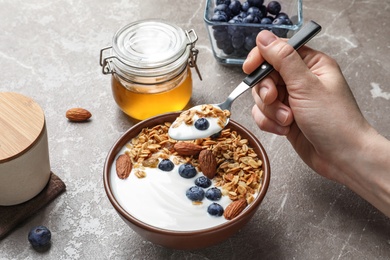 Photo of Woman eating tasty yogurt with berries and granola at table, closeup