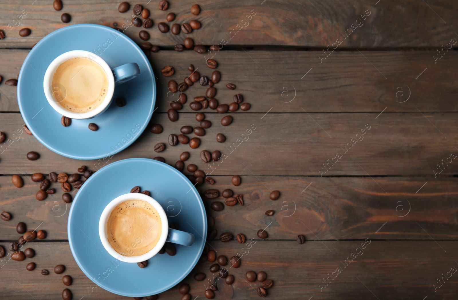 Photo of Cups of tasty espresso and scattered coffee beans on wooden table, flat lay. Space for text