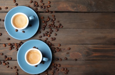 Photo of Cups of tasty espresso and scattered coffee beans on wooden table, flat lay. Space for text