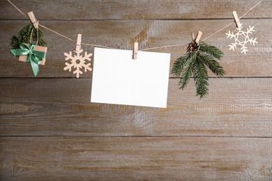 Blank Christmas card and festive decor on rope against wooden background. Space for text