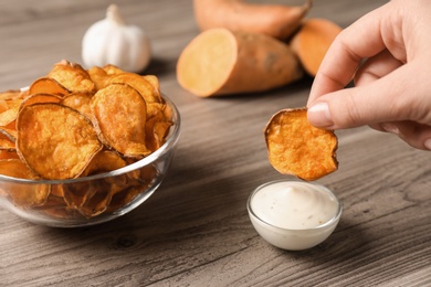 Woman dipping sweet potato chip into sauce on table, closeup