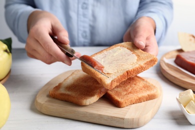 Woman spreading delicious quince paste on toast bread at white wooden table, closeup