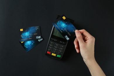 Woman with credit card using modern payment terminal on black background, top view