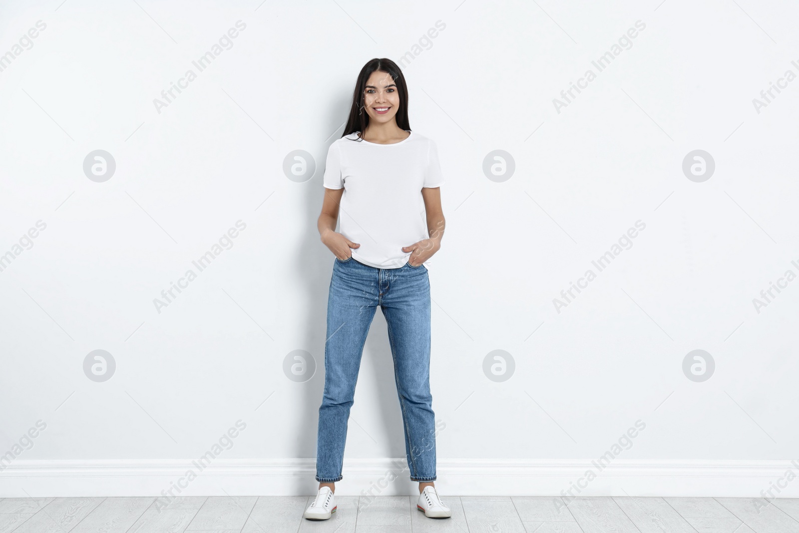 Photo of Young woman in stylish jeans near light wall