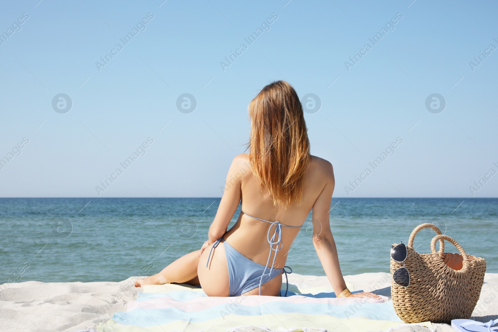 Photo of Woman with bag and other beach stuff on sand near sea, back view