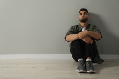 Sad man sitting on floor near light grey wall. Space for text