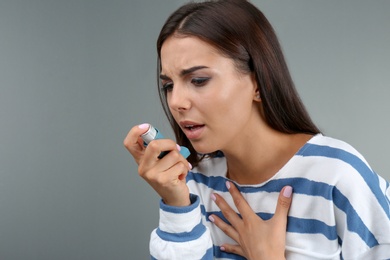 Photo of Young woman using asthma inhaler on color background