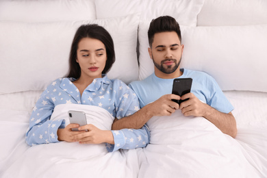 Photo of Distrustful young couple peering into each other's smartphones in bed at home, above view