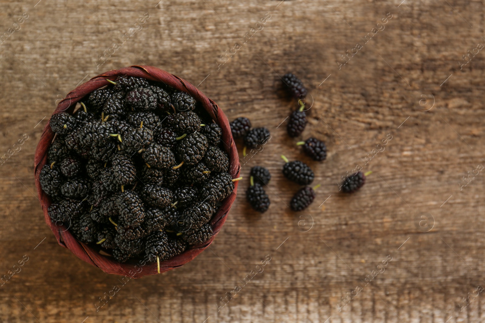 Photo of Wicker basket with delicious ripe black mulberries on wooden table, flat lay