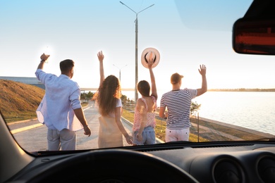 Group of friends near car outdoors at sunset, view through windshield. Summer trip