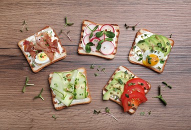 Different delicious sandwiches with microgreens on wooden table, flat lay