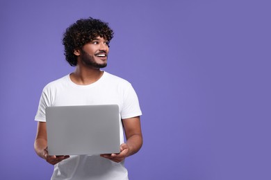 Photo of Smiling man with laptop on purple background, space for text
