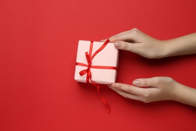 Photo of Woman holding beautiful gift box on red background, top view. Space for text