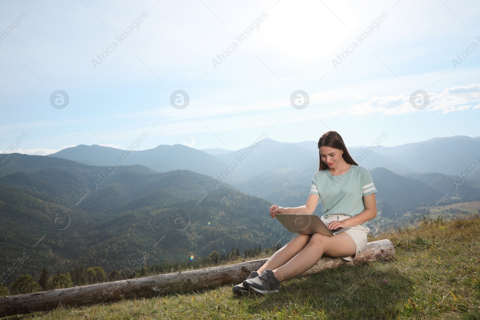 Photo of Young woman working with laptop in mountains on sunny day