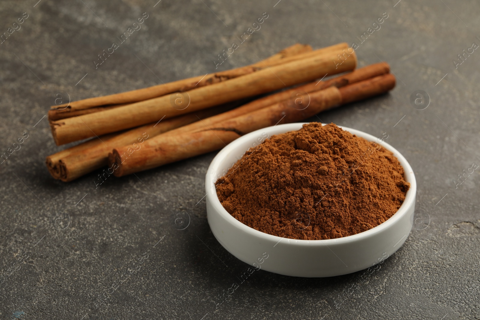 Photo of Bowl of cinnamon powder and sticks on grey table