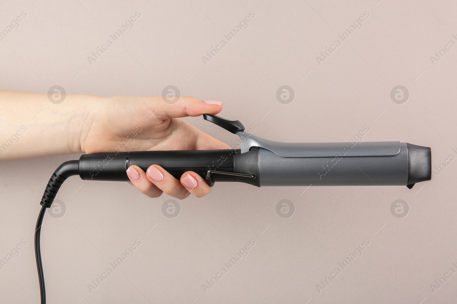 Photo of Hair styling appliance. Woman holding curling iron on light grey background, closeup