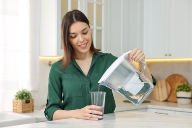 Woman pouring water from filter jug into glass in kitchen