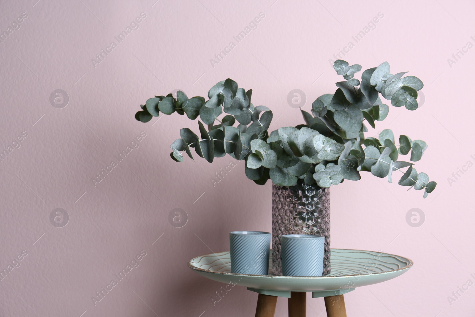 Photo of Eucalyptus branches and cups on table near pink wall