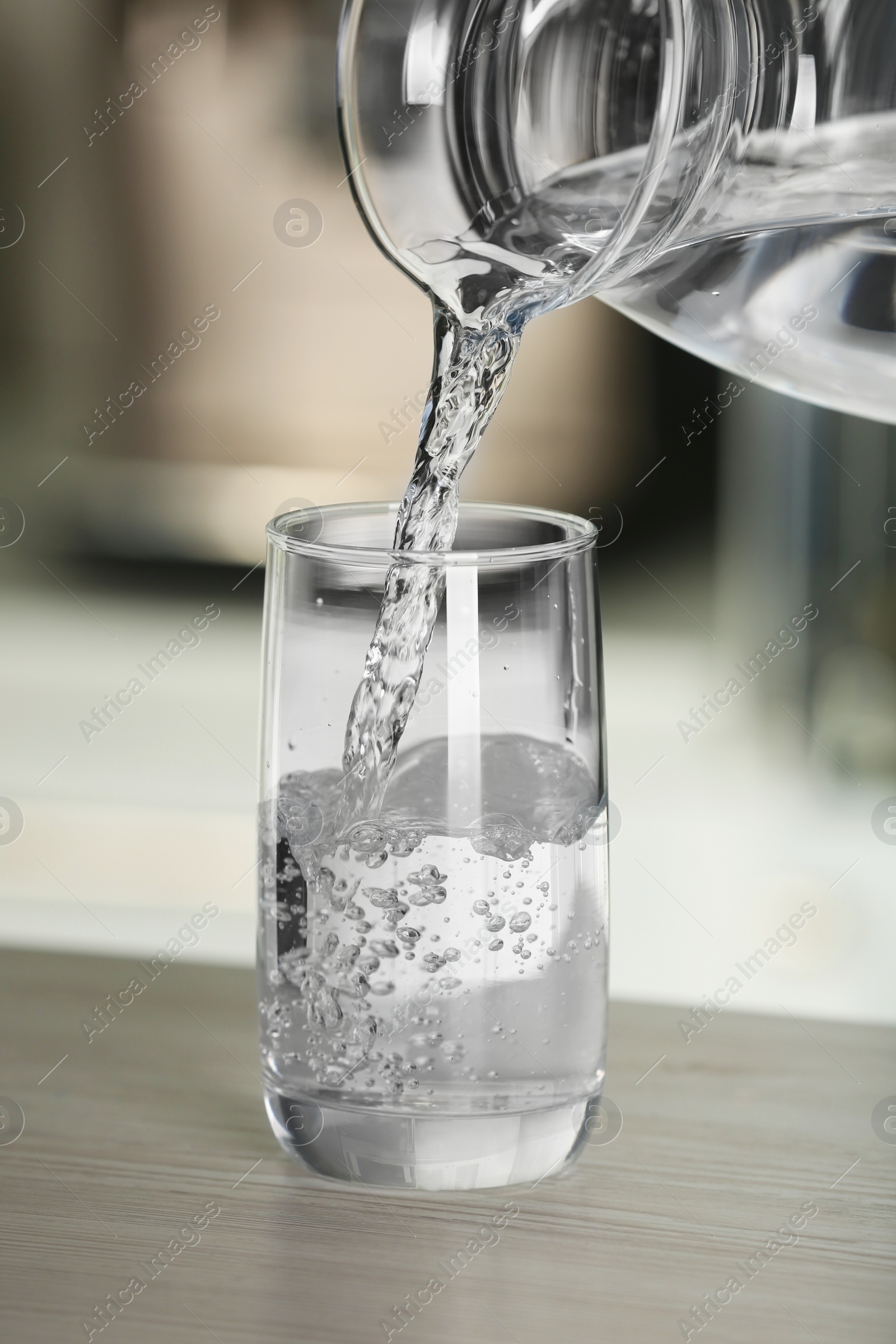 Photo of Pouring water from jug into glass on wooden table