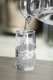 Photo of Pouring water from jug into glass on wooden table