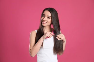 Beautiful smiling young woman with hair brush on color background