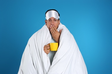 Man wrapped in blanket holding cup on blue background