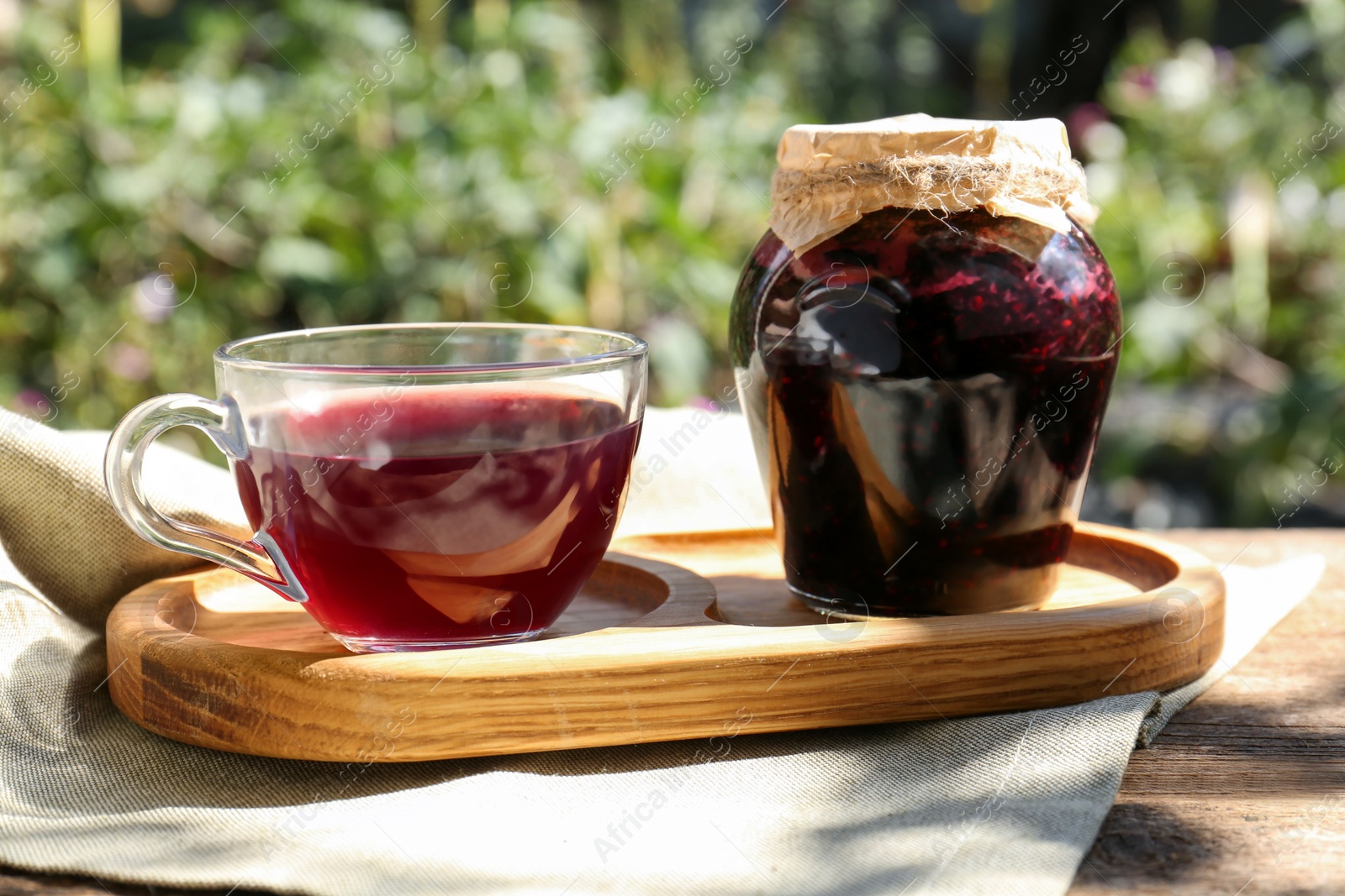 Photo of Elderberries (Sambucus) jam and glass cup of tea on table outdoors