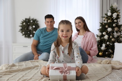 Happy family in room with Christmas tree, focus on daughter holding gift box