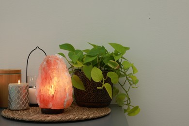 Himalayan salt lamp, houseplant and candles on grey table near light wall, space for text