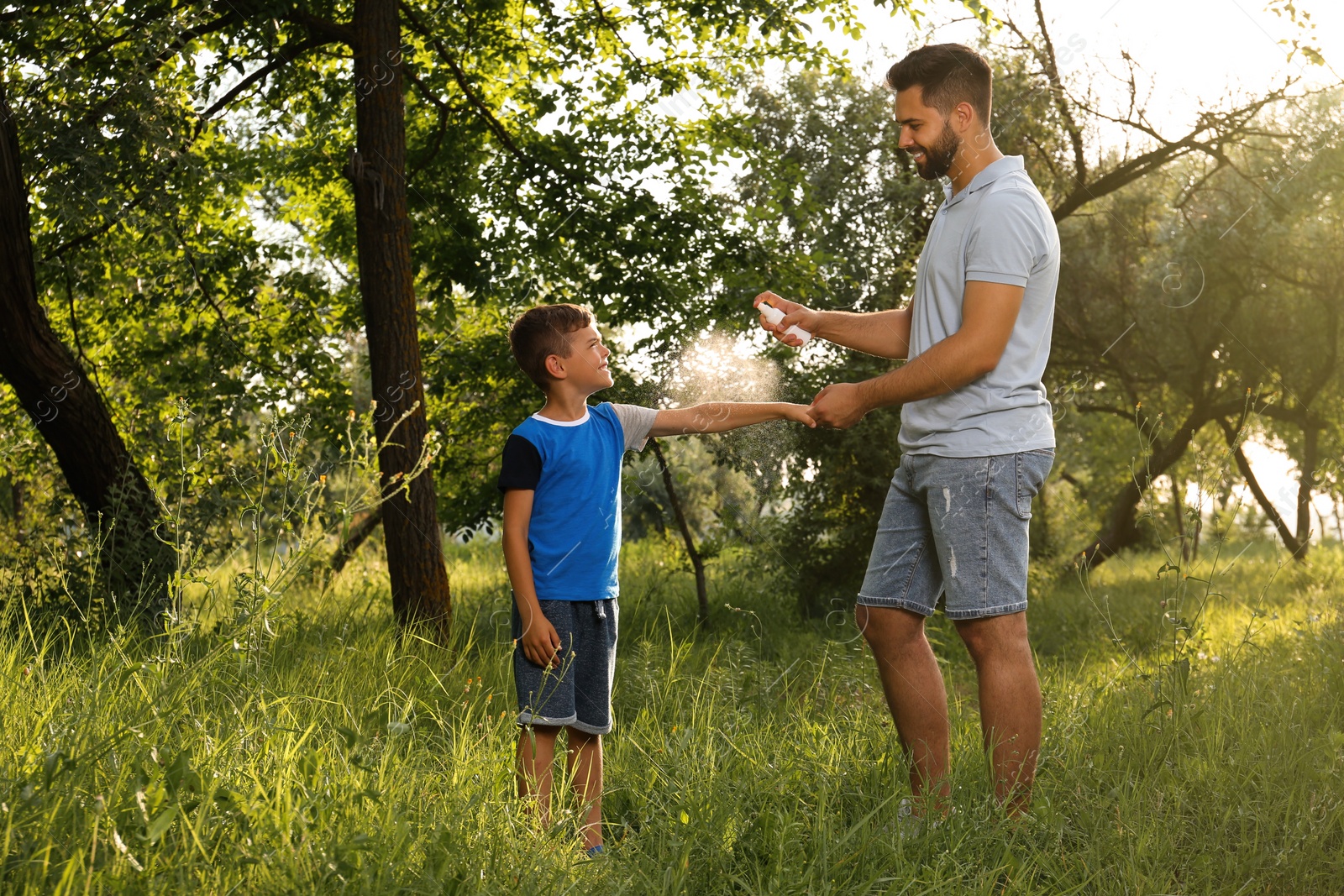 Photo of Man applying insect repellent on his son's arm in park. Tick bites prevention