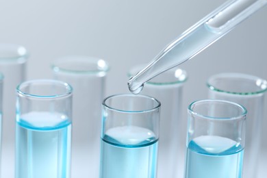 Dripping liquid from pipette into test tube on light background, closeup