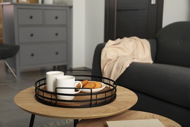 Photo of Tray with cups of hot drink and cookies on wooden table in living room, space for text. Interior design